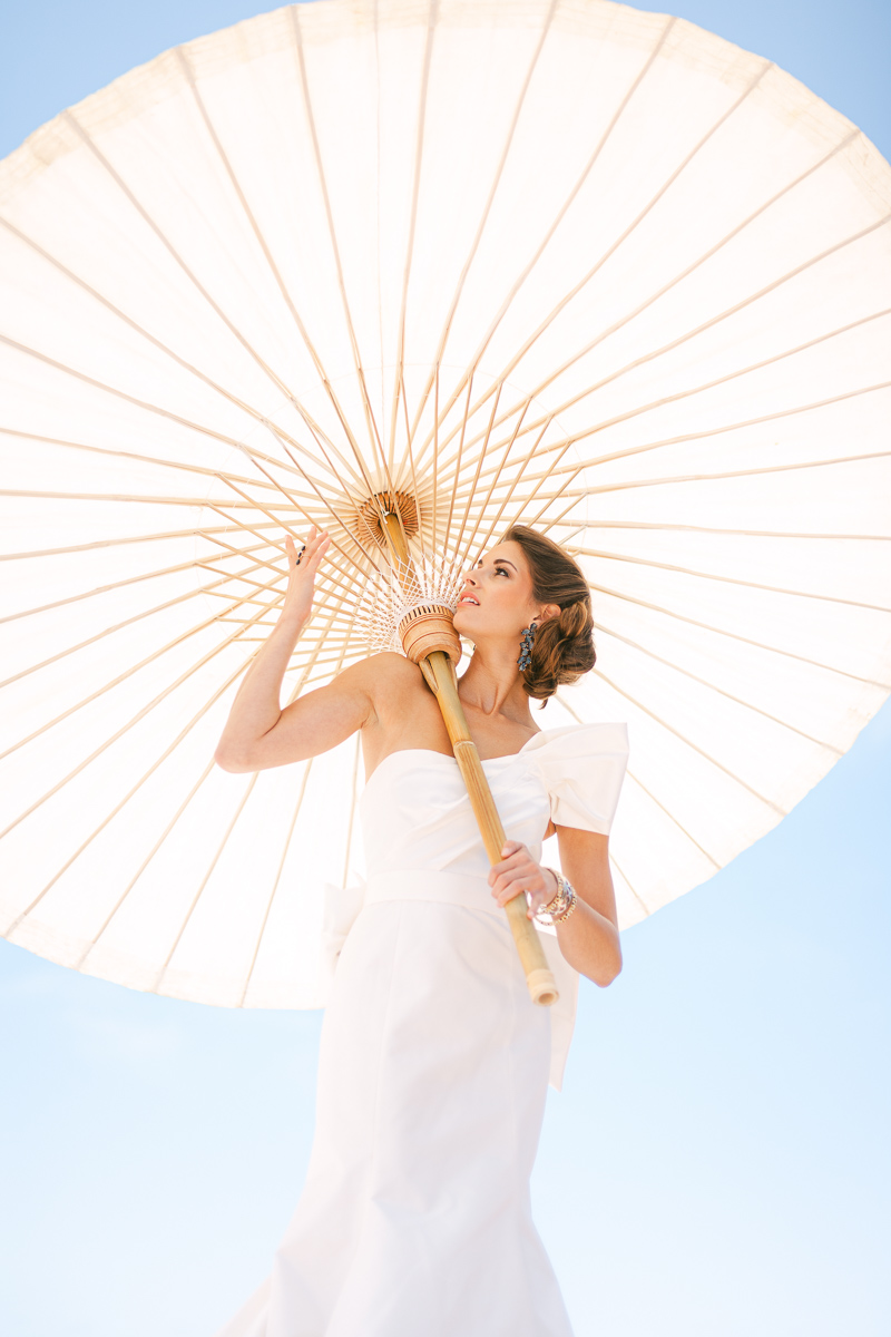 A bride stands under a large decorative umbrella in the sun during a wedding magazine photoshoot at Casa Romantica in San Clemente California